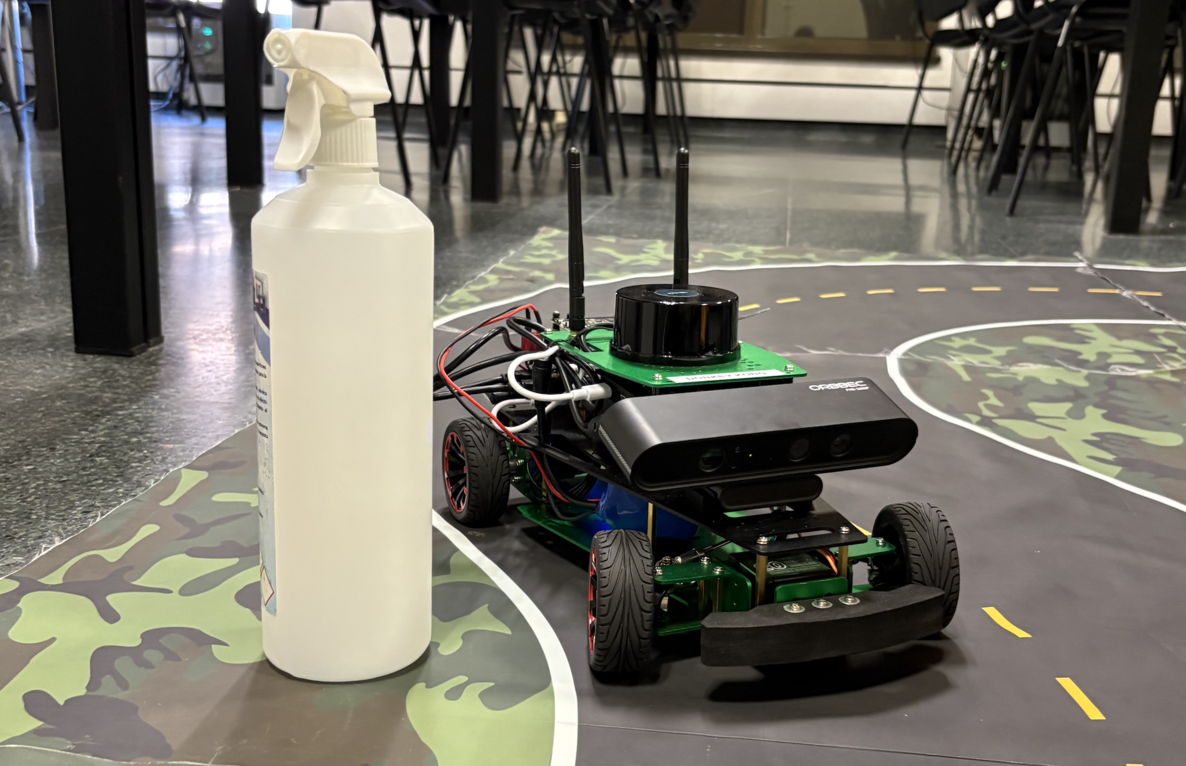 The RC car with LiDAR and RGB camera on a taped circuit, next to a plastic bottle used as an obstacle